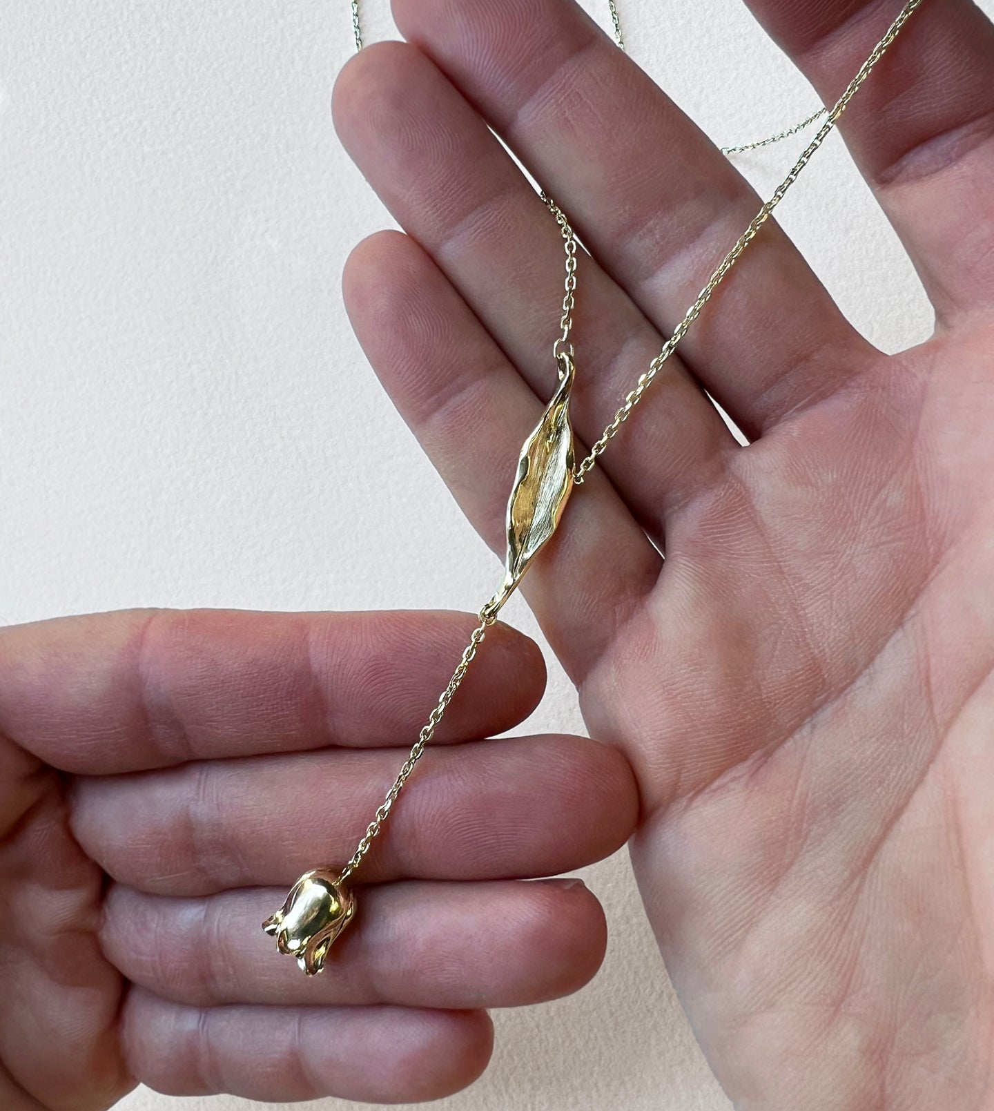 Close-up of the gold lily-of-the-valley flower and carved leaf on a delicate diamond-cut chain