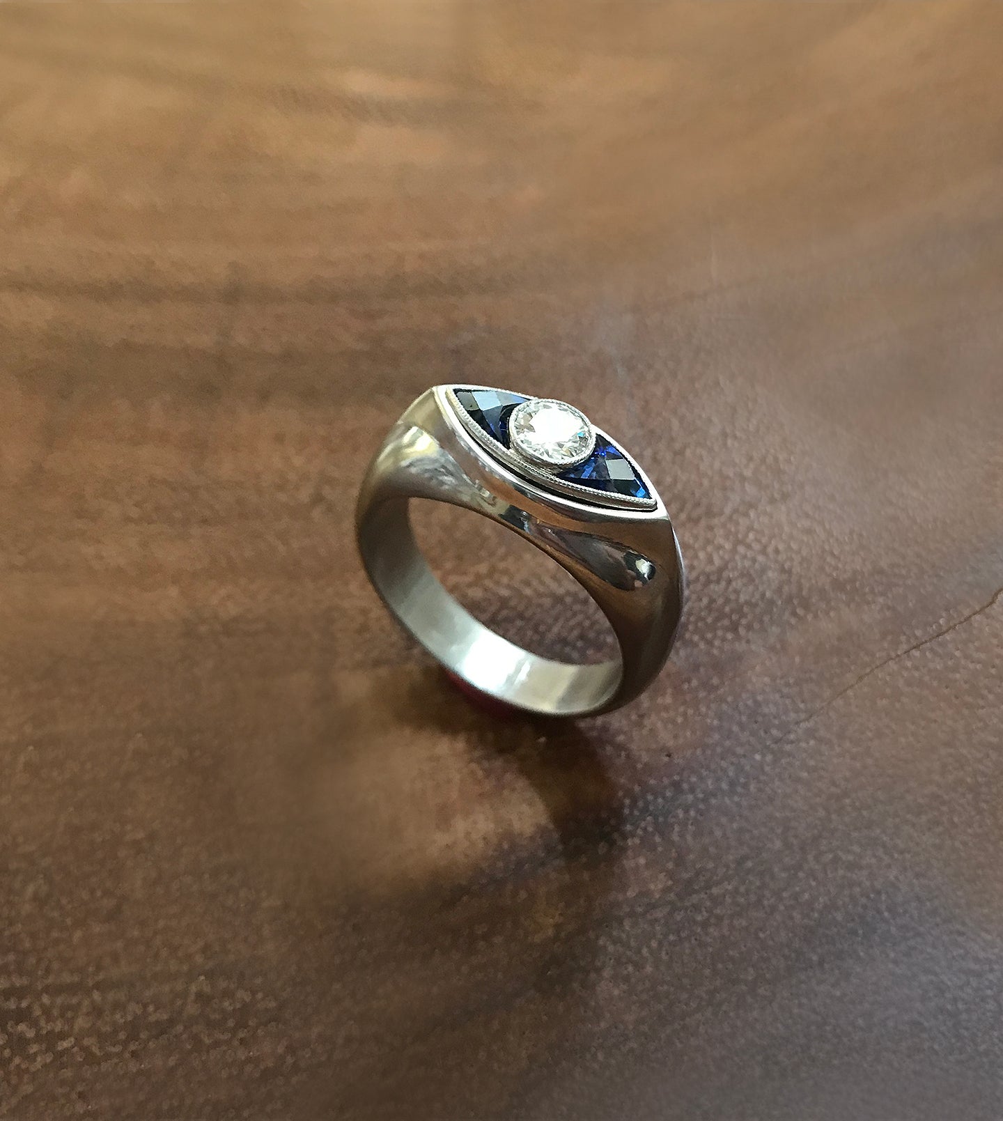 Platinum signet ring with an eye motif—a central diamond flanked by blue sapphires forming the eye