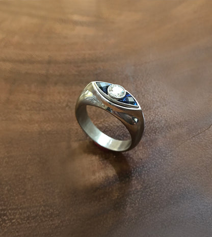 Platinum signet ring with an eye motif—a central diamond flanked by blue sapphires forming the eye
