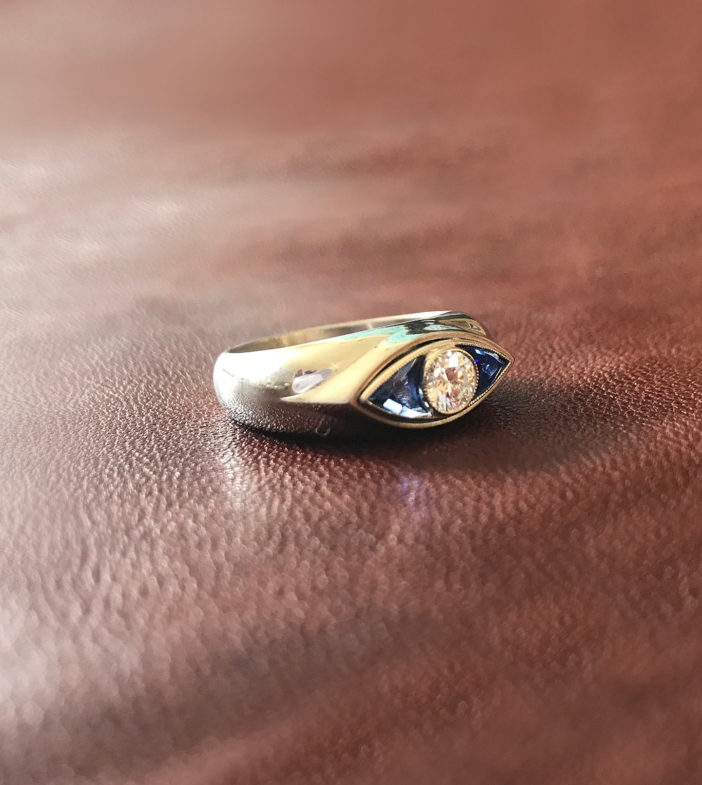 Close-up of the eye motif with a central diamond and blue sapphires in a platinum signet