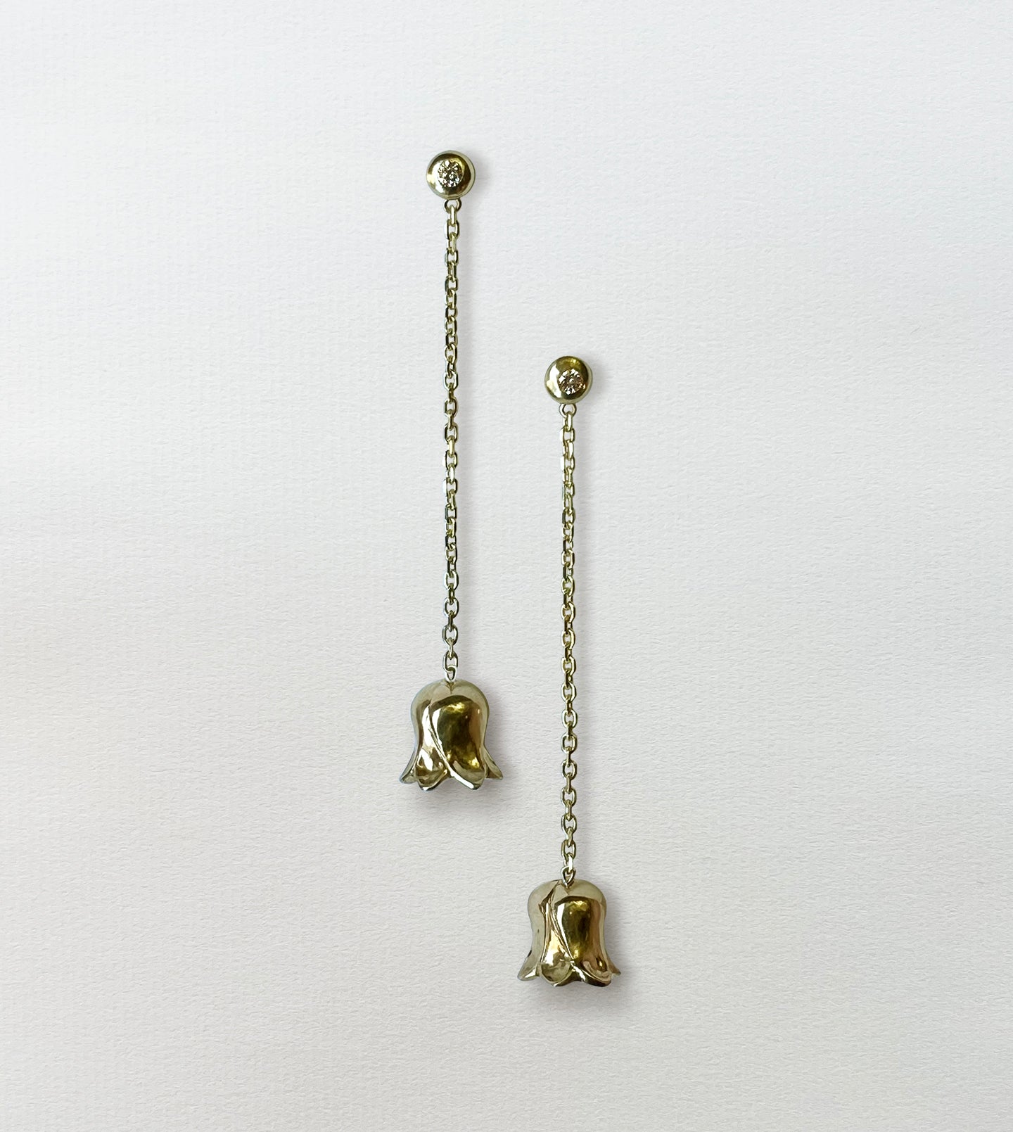 Pair of gold lily-of-the-valley drop earrings on paper, diamond studs with chains and bell flowers