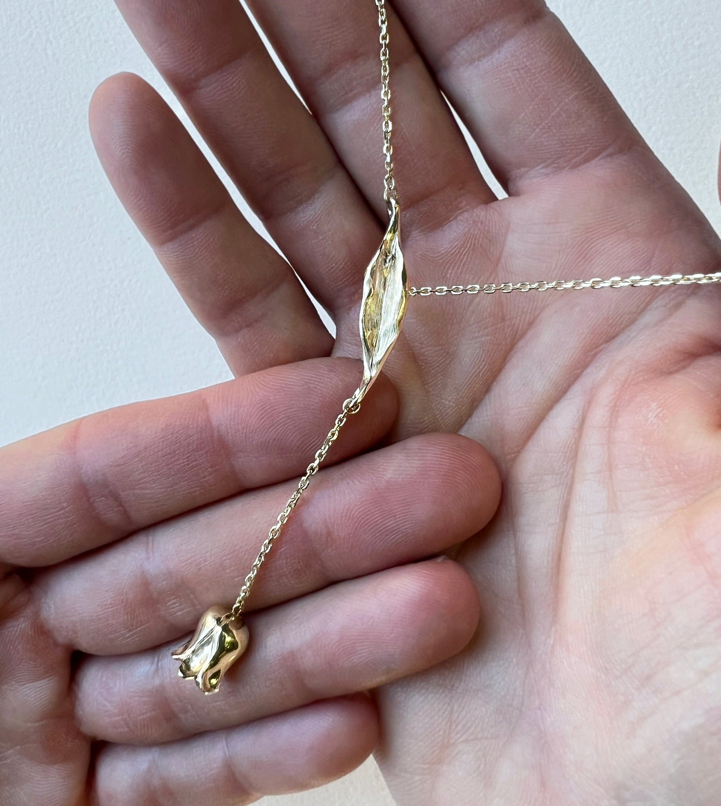 Hand-carved gold lily-of-the-valley lariat held in hands, leaf and tiny bell flower on a fine gold chain