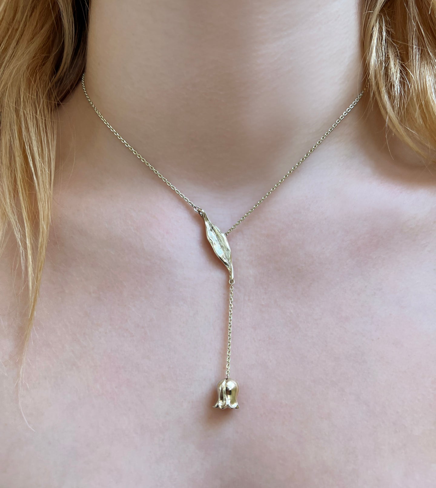 Gold lily-of-the-valley lariat necklace worn on the neck, a carved leaf with a bell flower dropping below
