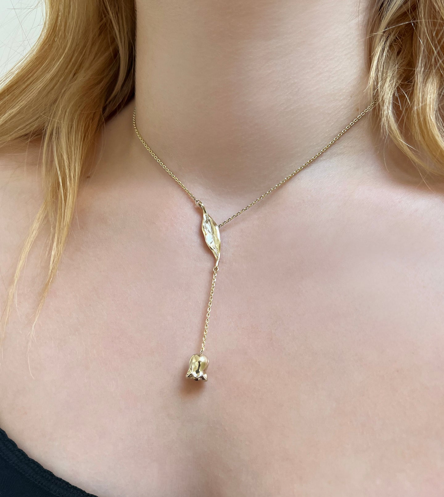 Gold lariat necklace on the neck, alternate view of the lily-of-the-valley leaf and flower drop