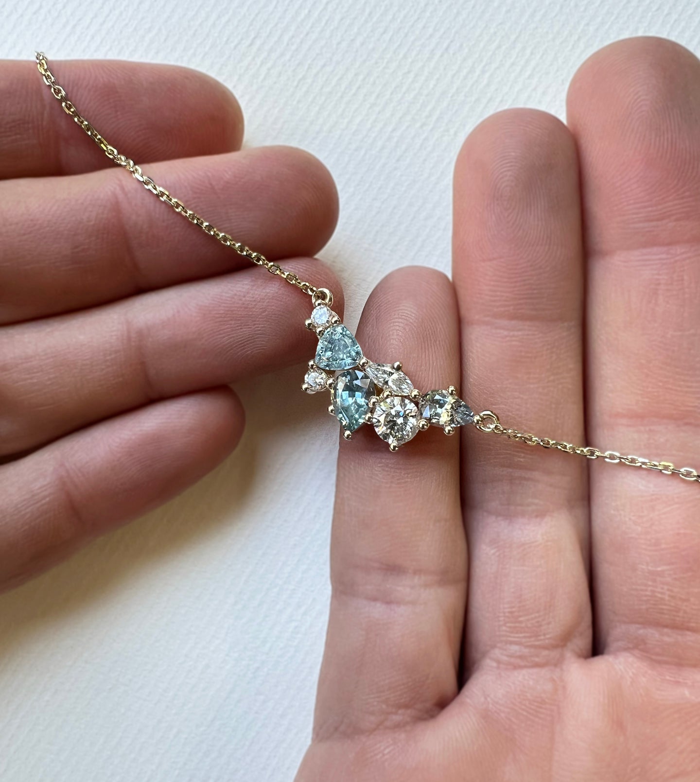 Custom Montana sapphire gem cluster necklace held in hands, showing the organic gold setting