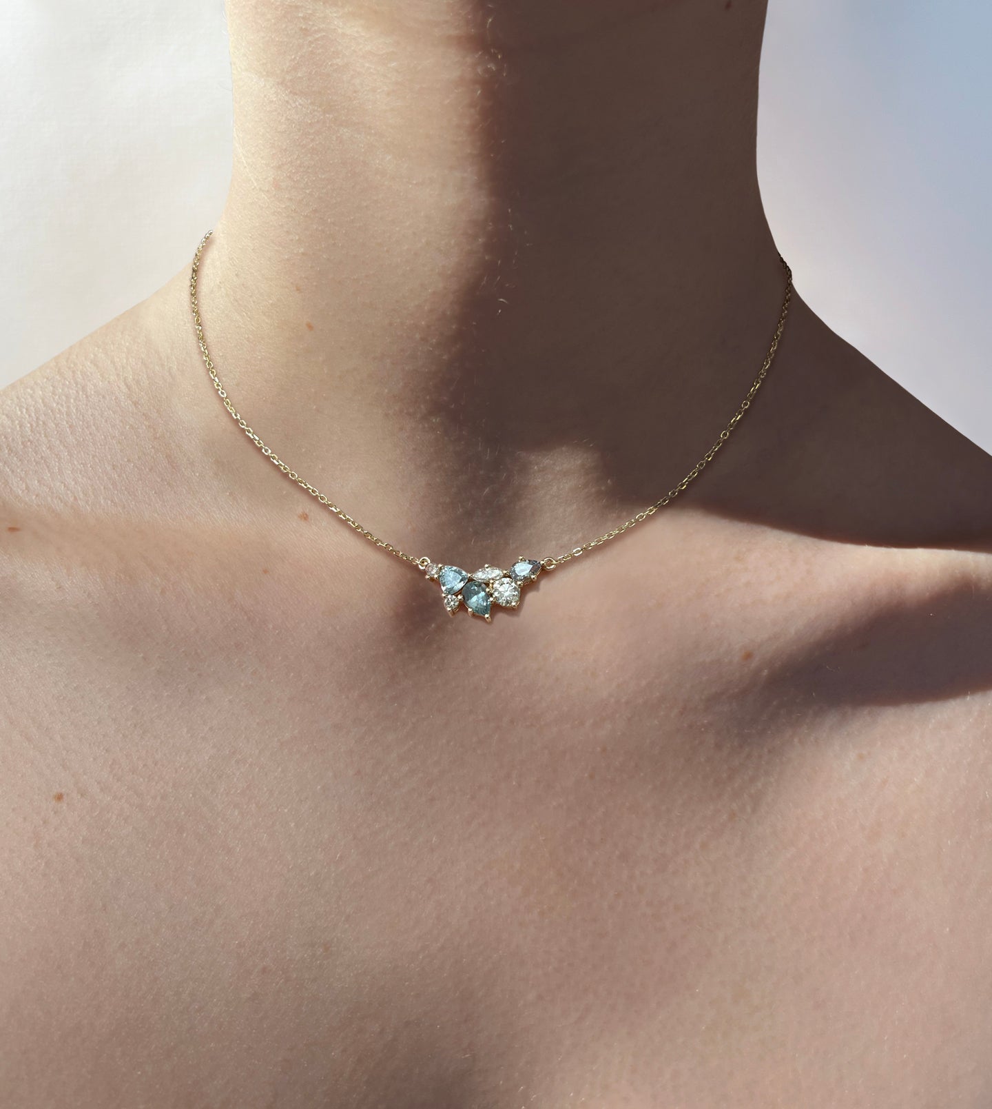 Montana sapphire and diamond cluster necklace in yellow gold worn on the neck on a fine cable chain