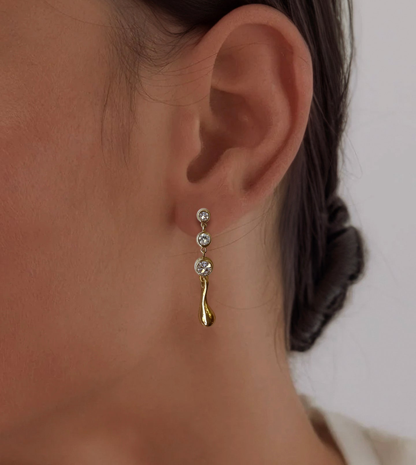 Gold diamond drop earring worn on the ear, graduated bezel-set diamonds cascading to a gold waterdrop