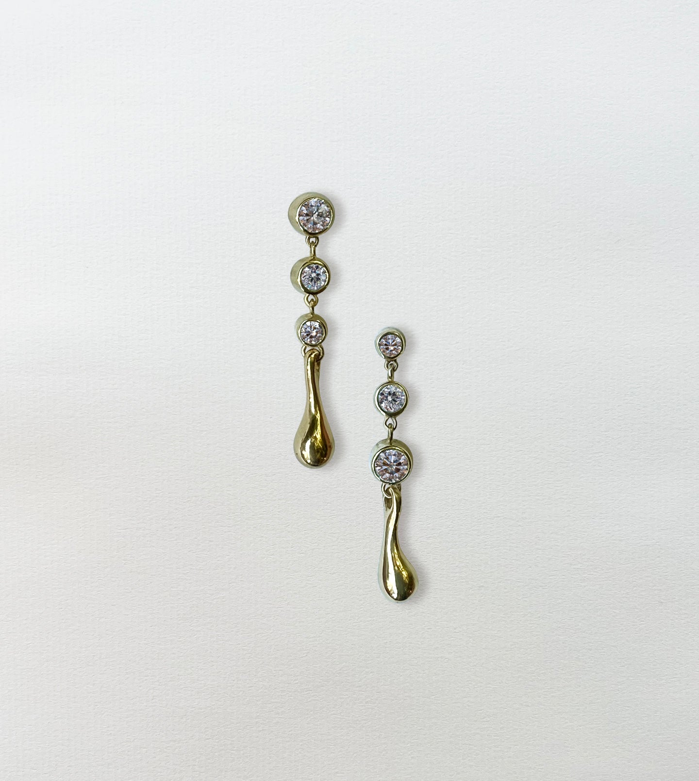 Pair of gold diamond waterdrop drop earrings on paper, graduated bezel-set diamonds ending in a gold teardrop