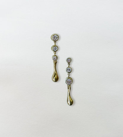 Pair of gold diamond waterdrop drop earrings on paper, graduated bezel-set diamonds ending in a gold teardrop