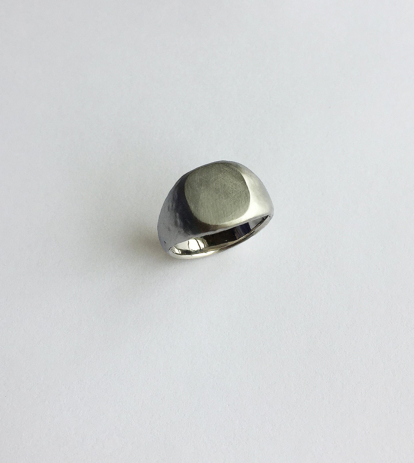 Palladium signet ring with a simple brushed face and polished band, on a pale background