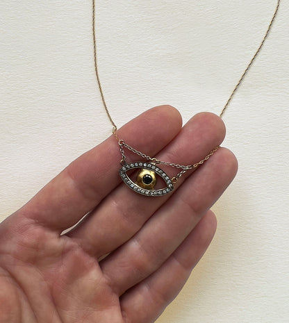 Gold and darkened white gold evil eye pendant necklace with a pavé eye outline and dark center stone