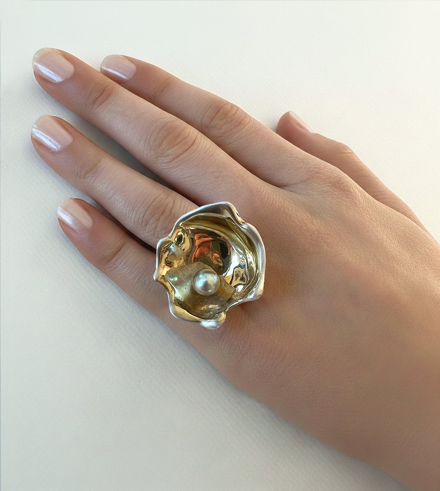 Large oyster cocktail ring with a pale gray pearl in a gold-and-silver shell, worn on a hand