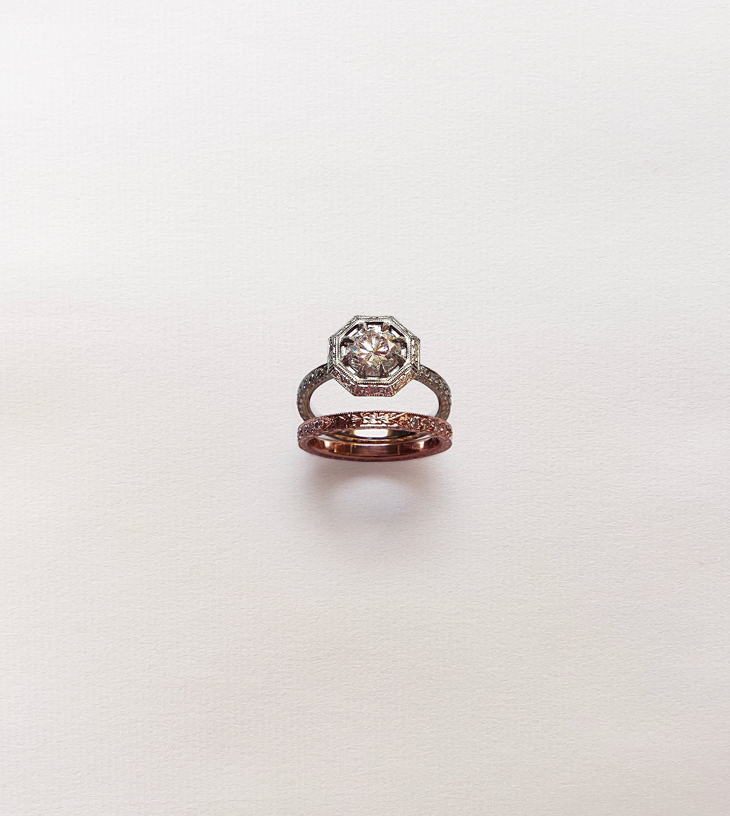 Octagonal engagement ring with a round diamond shown above its hand-engraved rose gold matching band