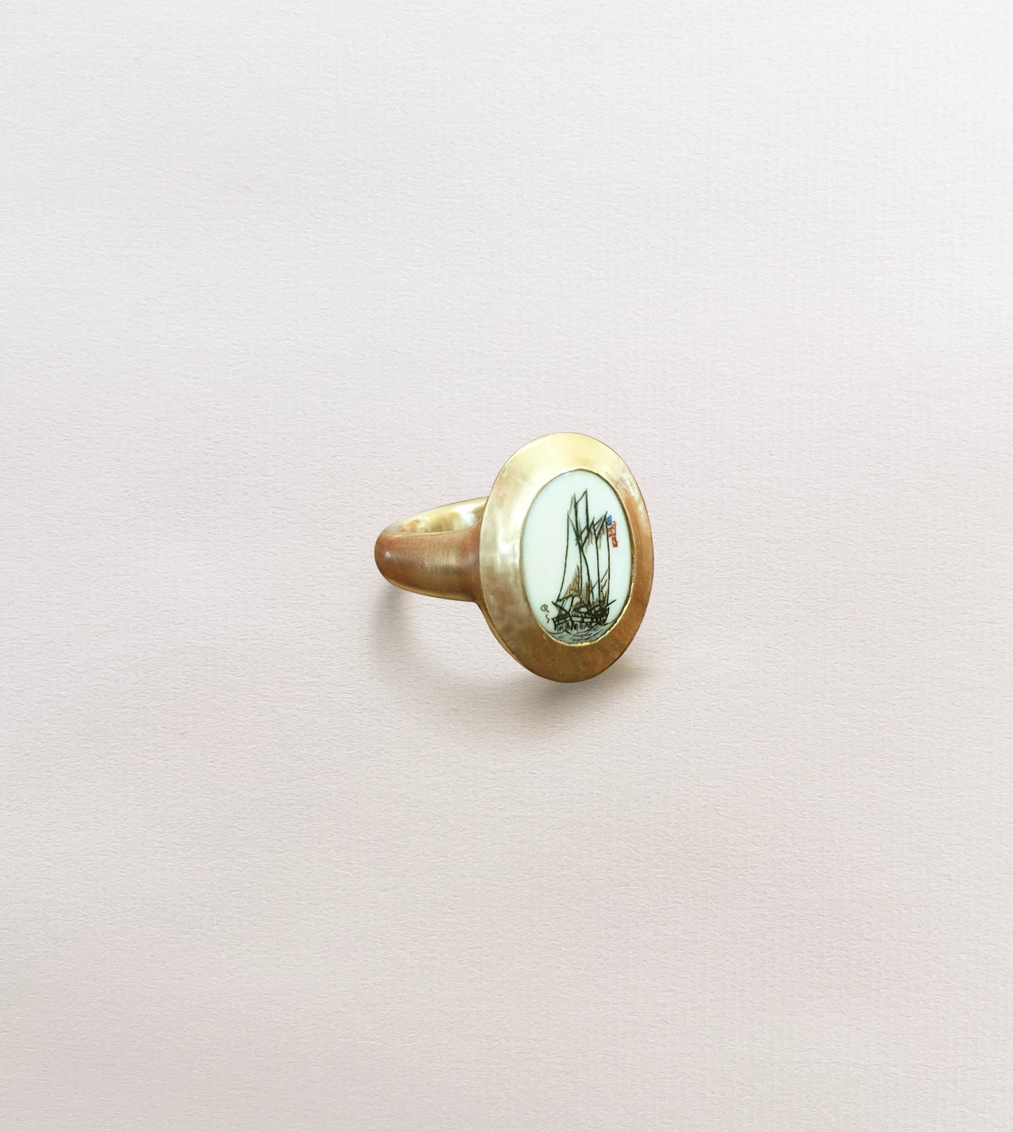 Hand-hammered yellow gold ring framing an oval scrimshaw of a sailing ship in a wide bezel