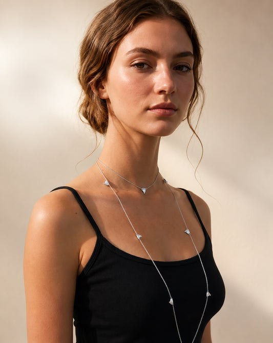 Woman wearing a long, delicate thorn necklace against a neutral background