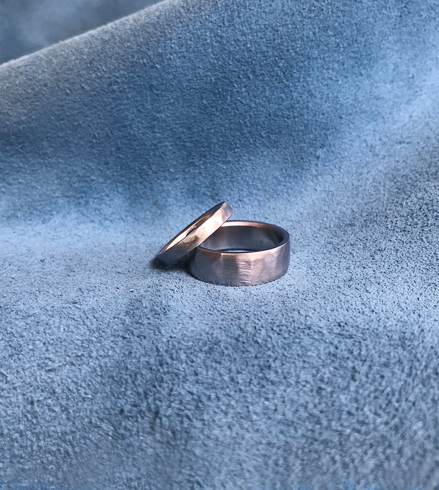 Hammered platinum wedding band pair resting on blue suede, showing the wide and narrow rings