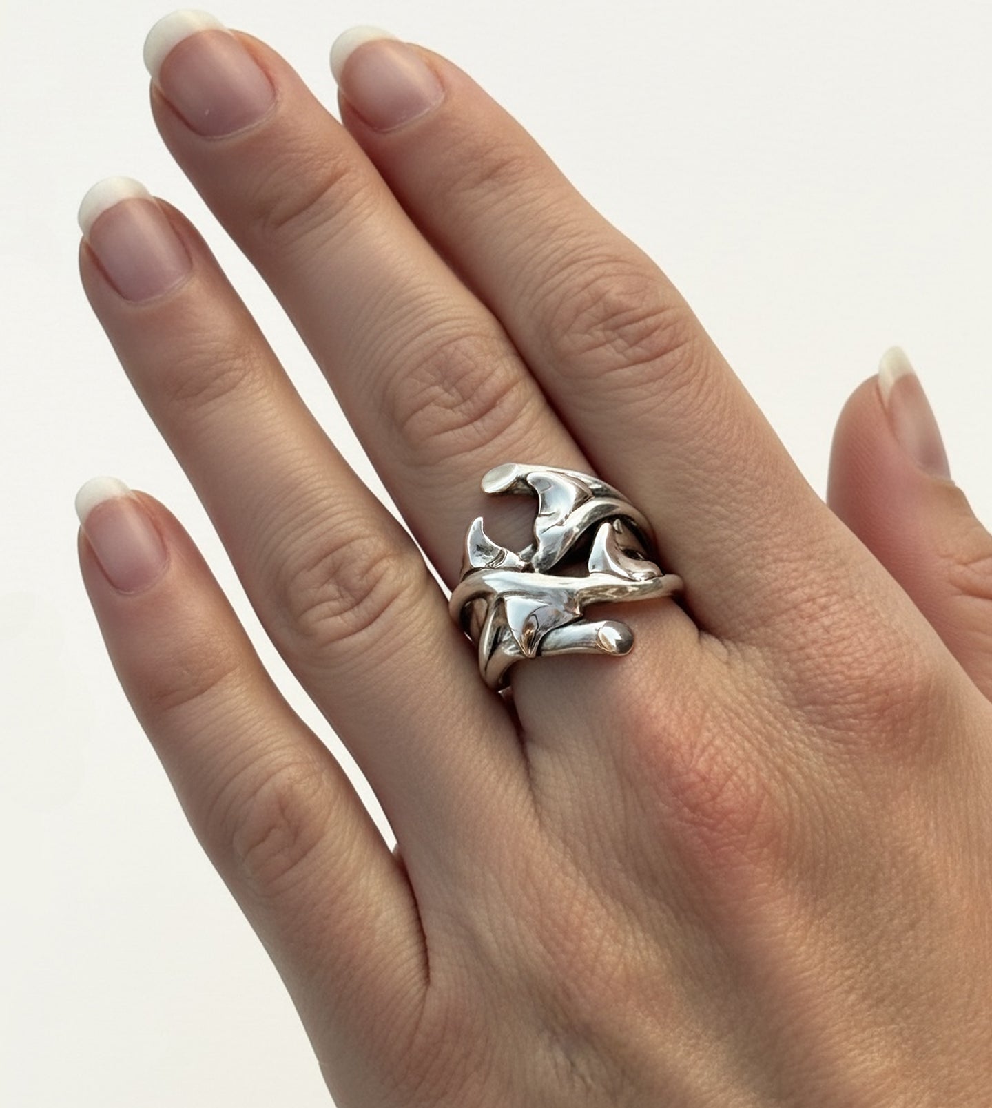 Shiny sterling silver rose thorn statement ring on woman's finger, catching light across its sculpted form