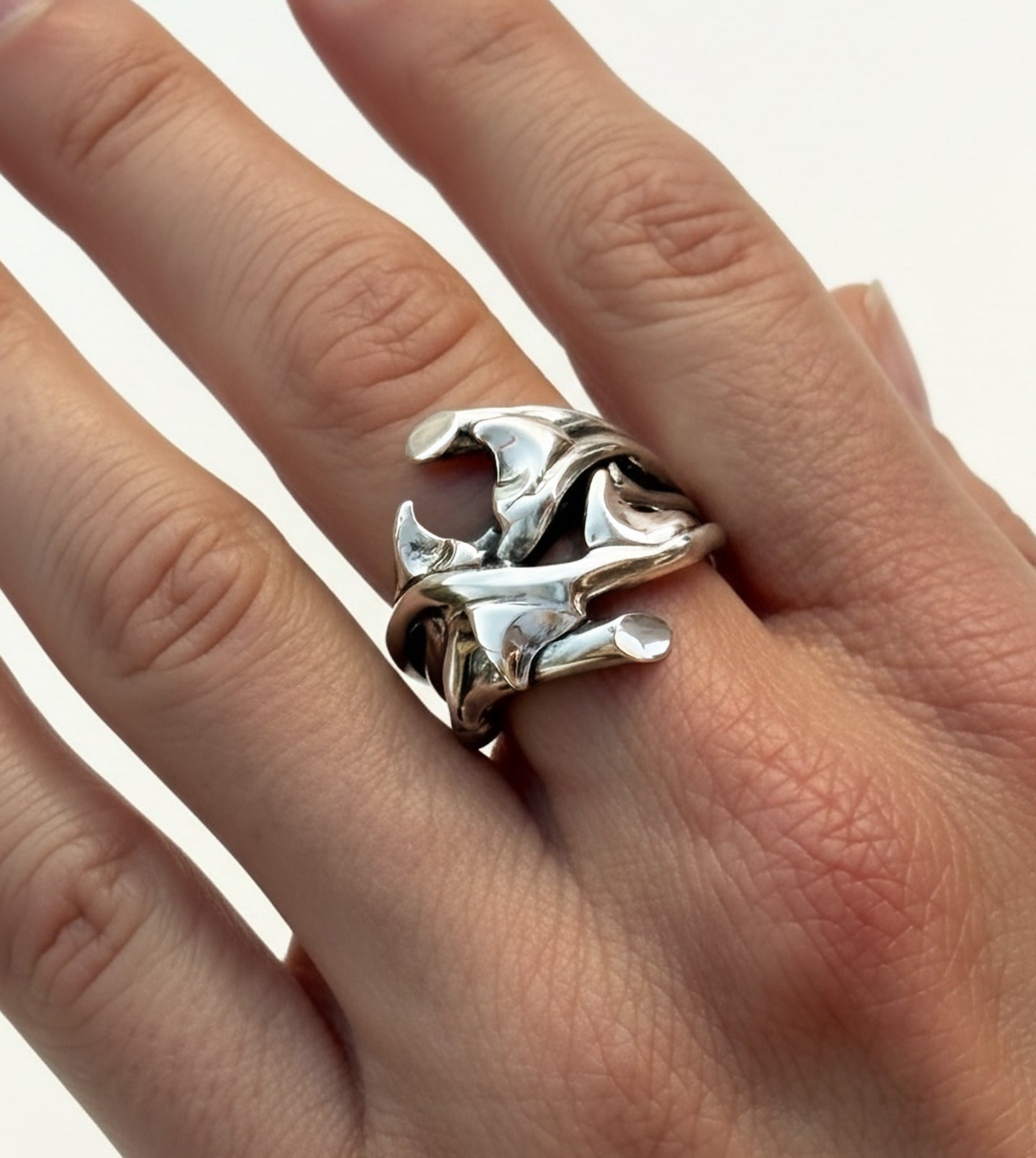 Closeup of sterling silver rose thorn ring with shiny finish, worn on hand to show scale and sculptural detail
