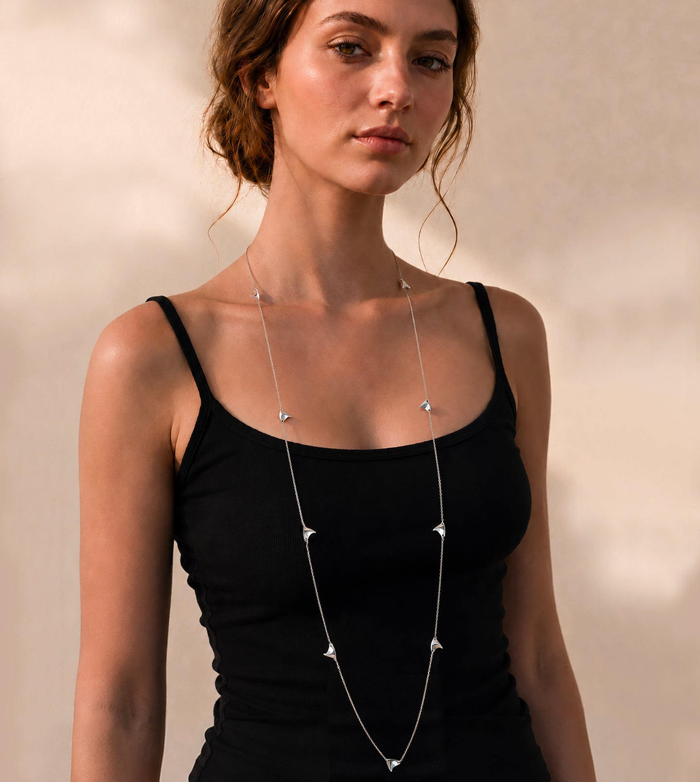 Woman wearing a long, delicate sterling silver thorn necklace against a neutral background