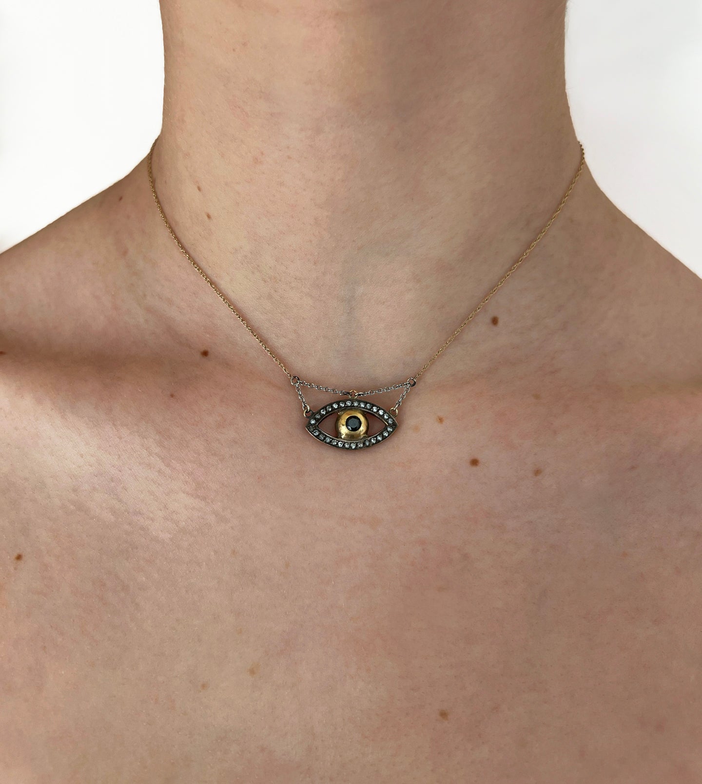 Gold evil eye necklace worn on the neck, eye-shaped pendant with pavé outline and dark center stone