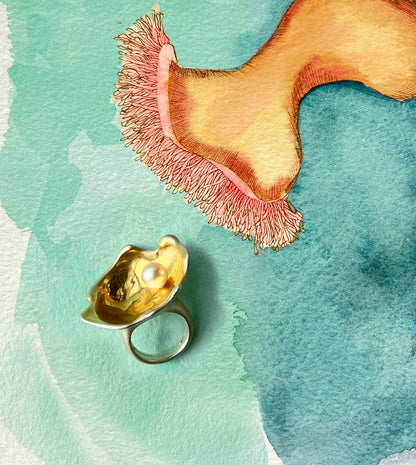 Oyster-shell cocktail ring cradling a pale gray pearl, shown on a sketchbook