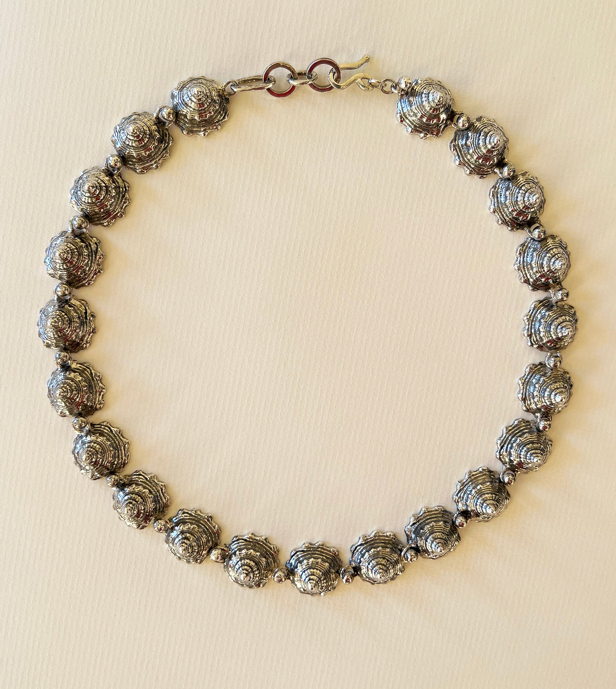 Sterling silver whelk shell spire collar necklace laid flat on paper