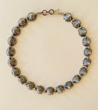 Sterling silver whelk shell spire collar necklace laid flat on paper