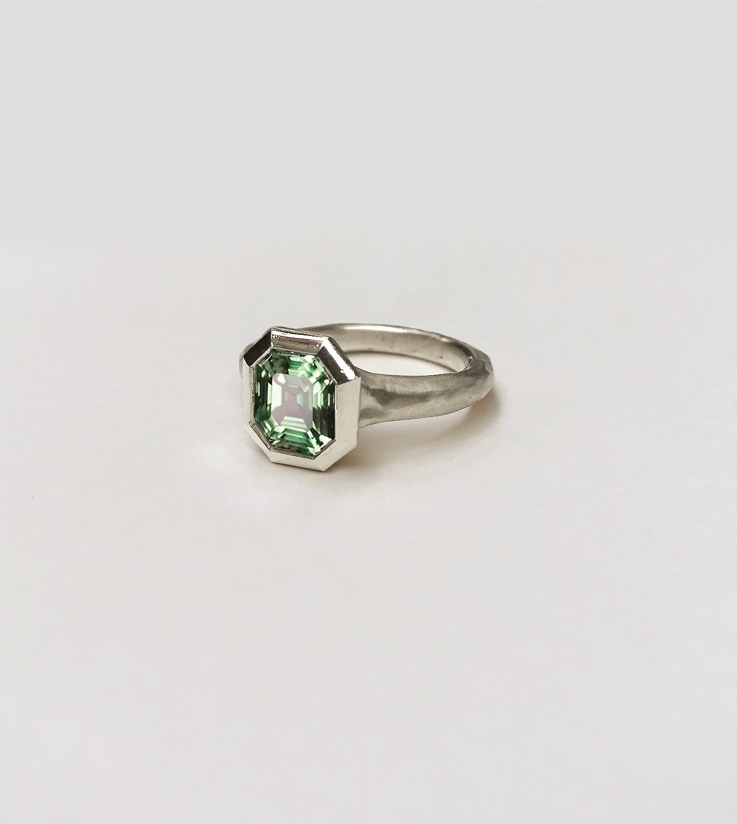 Hand-carved platinum ring with an emerald-cut green sapphire in a wide sculptural bezel