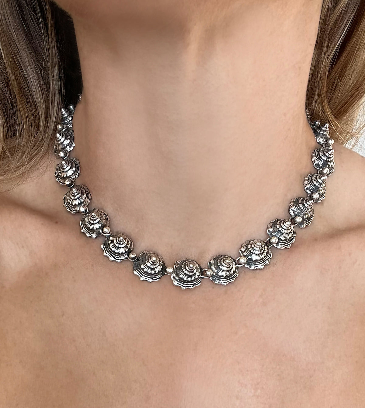 Blackened sterling silver shell necklace worn as a collar, interlocking whelk shell spires around the neck