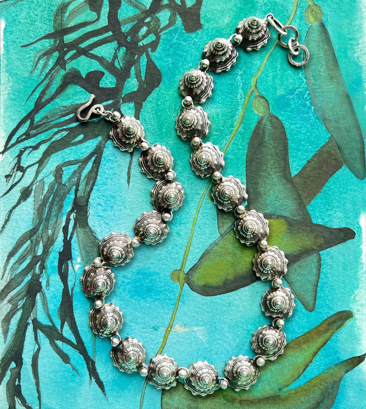 Sterling silver shell spire necklace shown on a sketchbook, interlocking blackened whelk shells