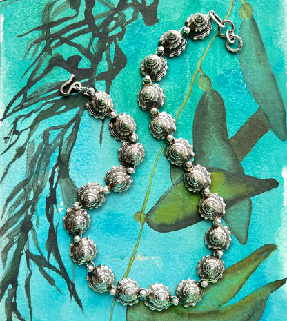 Sterling silver shell spire necklace shown on a sketchbook, interlocking blackened whelk shells