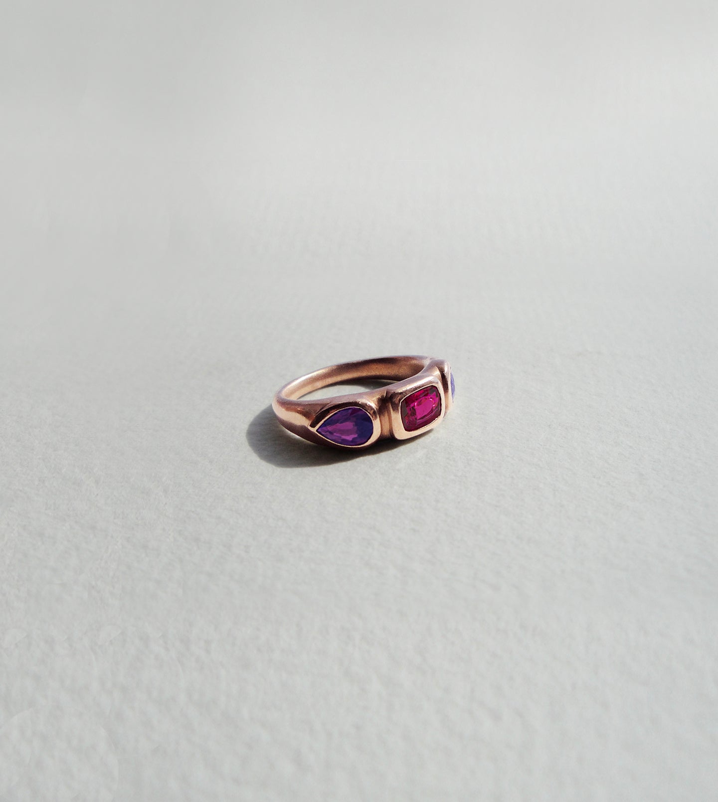 Rose gold signet-style ring with a central ruby flanked by purple sapphires in low bezels