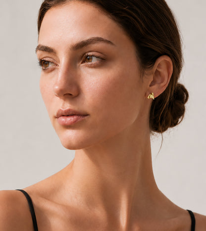 Close-up of a woman wearing a yellow gold rose thorn earring against a neutral background